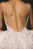 A close-up back view of a woman wearing a white lace bridal dress with an open back and layered delicate rose gold chain backlaces draped across her skin.