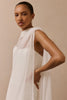 A woman wearing a flowing white draped dress or wrap against a plain beige studio background.