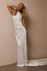 A woman modeling a floor-length white satin gown with a draped neckline and a long train, posed against a plain beige wall_XS_