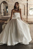 A woman wearing a strapless white ball gown wedding dress with a structured bodice and full skirt