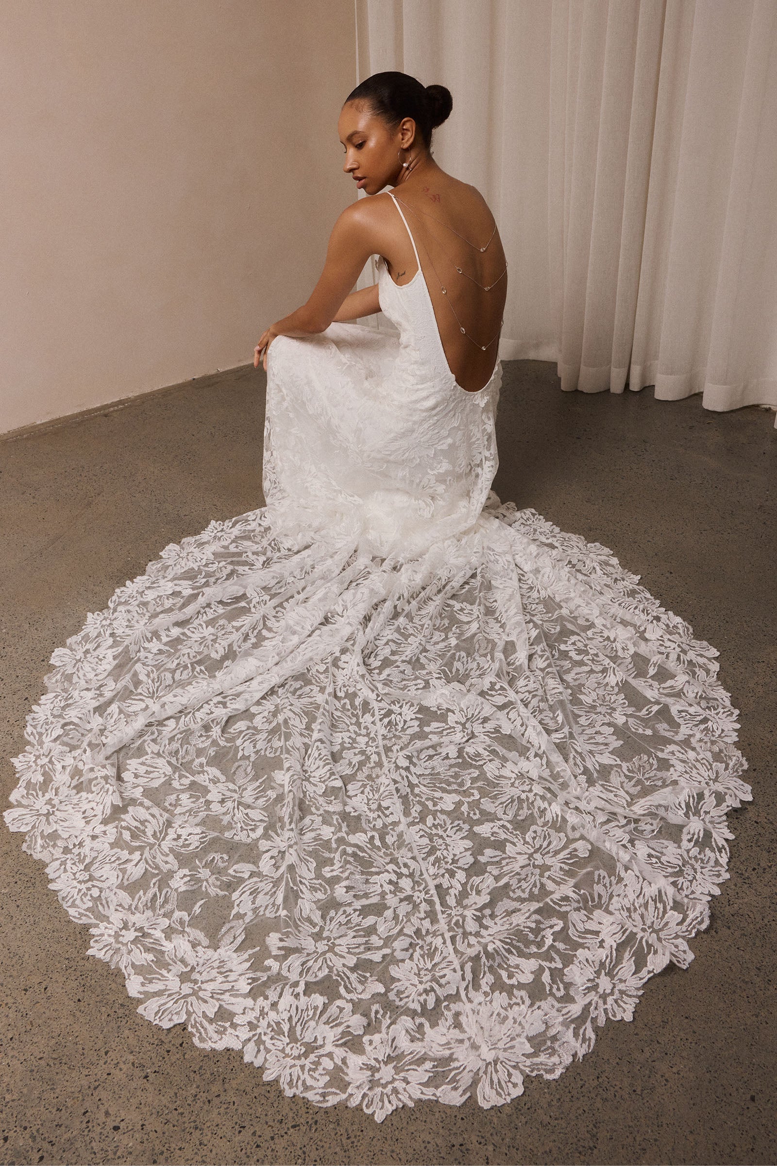 woman wearing a white lace backless dress with thin straps and delicate chain jewellery across her back_XS_