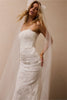 A woman wearing a strapless white lace wedding gown with a long train